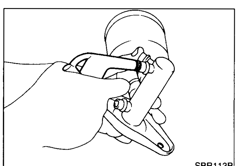 Illustration showing technician applying compressed air through the fluid outlet to remove the secondary piston assembly while wearing protective gear.