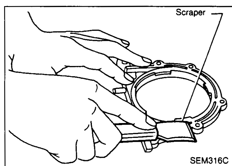 Hand using a scraper on the rear oil seal retainer to remove traces of old liquid gasket. Callout: 'Scraper'.