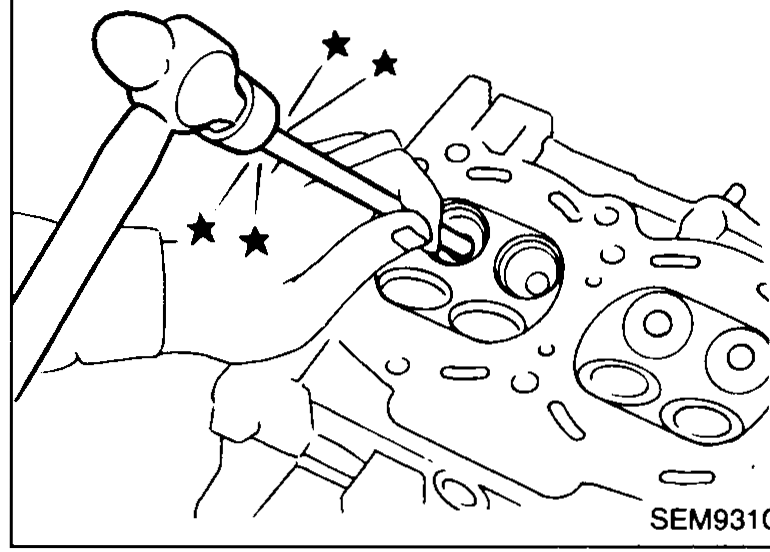 Cylinder head submerged/heated in an oil bath in a heated tank, oil arrow pointing at the bath. Used to heat the head to 110–120°C to release the valve guides for removal.