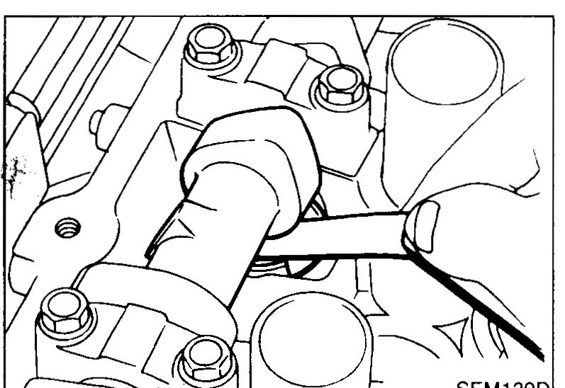 Hand using a feeler gauge between cam lobe and valve lifter shim on the cylinder head to measure valve clearance. View shows cam and lifter from above with feeler blade inserted.
