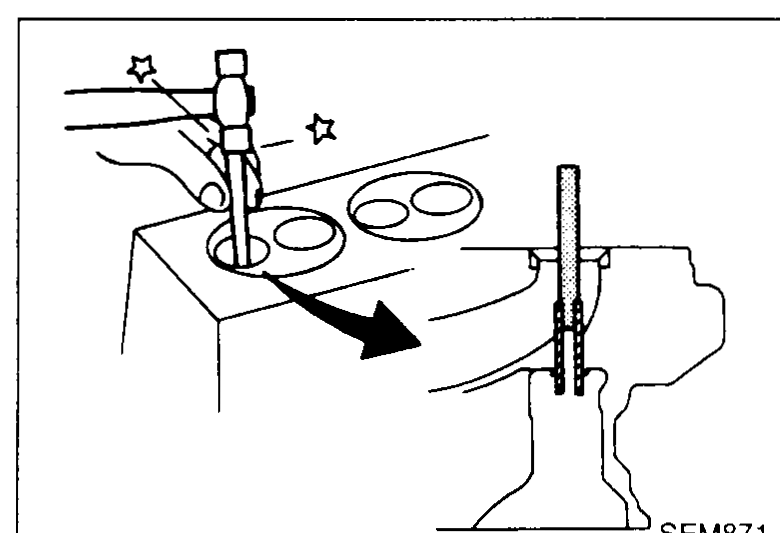 Cylinder head in oil bath at 150–160°C with hand using a press/hammer driver to drive out a valve guide downwards — illustrates valve-guide replacement step 2.