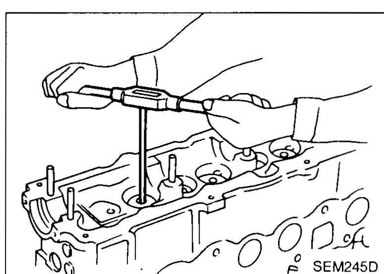 Cylinder head on bench with hand using a T-handle reamer to ream the valve-guide bore in the head — illustrates valve-guide replacement step 3.