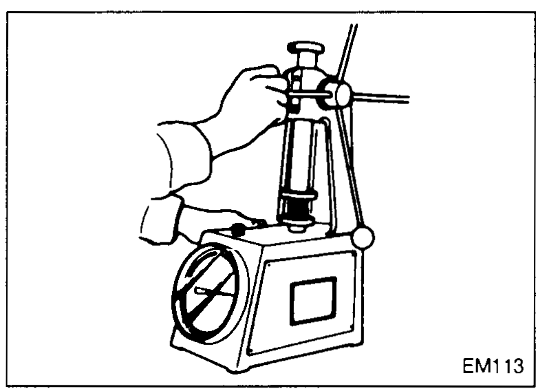 Cross-section of cylinder head with intake and exhaust valves seated; arrows show measurement from the cylinder head deck surface down to the valve head crowns to verify recess distance. Labels 'Intake' and 'Exhaust' on the left.