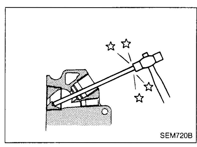 Cylinder head on bench with a long lever-style remover being inserted through a glow-plug bore to push the combustion chamber out — illustrates combustion-chamber removal (step 3).