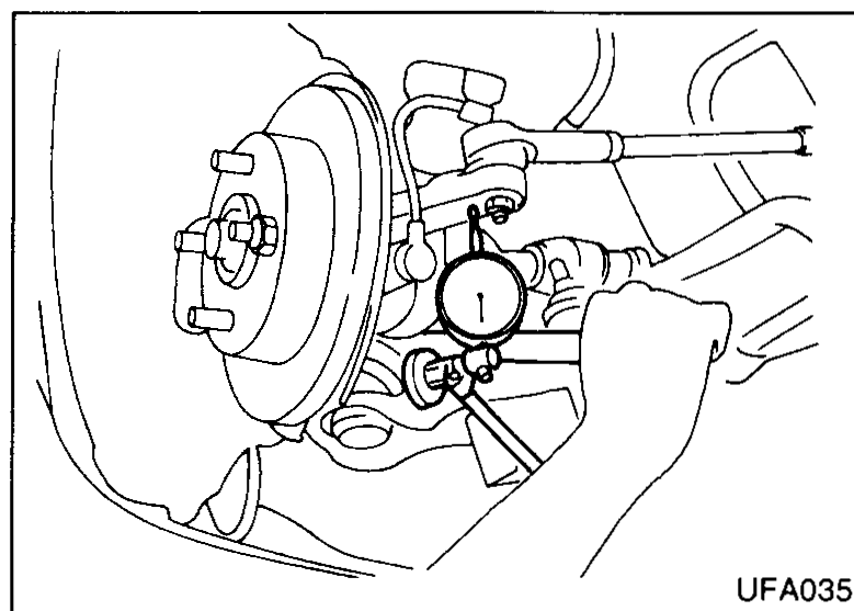 Photo of a dial indicator clamped to the transverse link with its tip resting on the lower edge of the steering knuckle while a pry bar is placed between the transverse link and drive shaft to check suspension ball-joint end play.