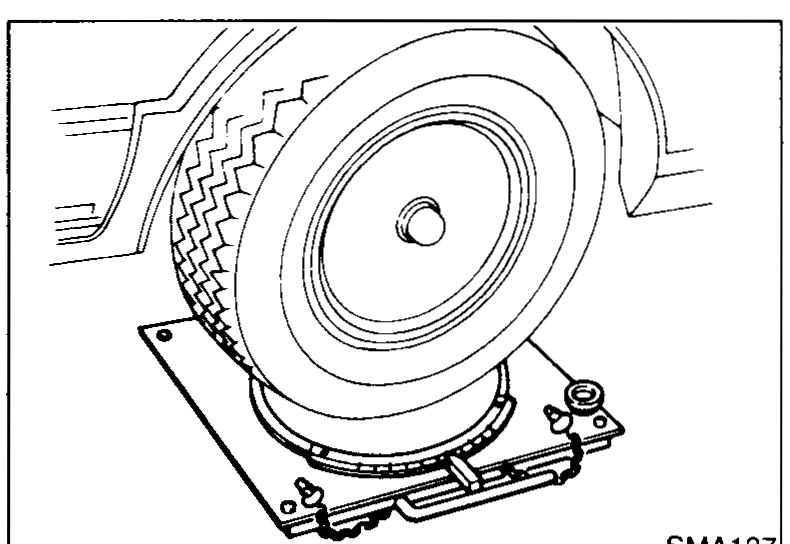 Perspective view of a front tire resting on a turning-radius gauge plate, used to measure the wheel turning angle.