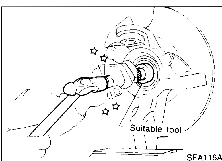 Photo of a dial indicator clamped to the hub face with its tip on the hub centre. An arrow indicates axial-play measurement direction while checking wheel-bearing axial end play.
