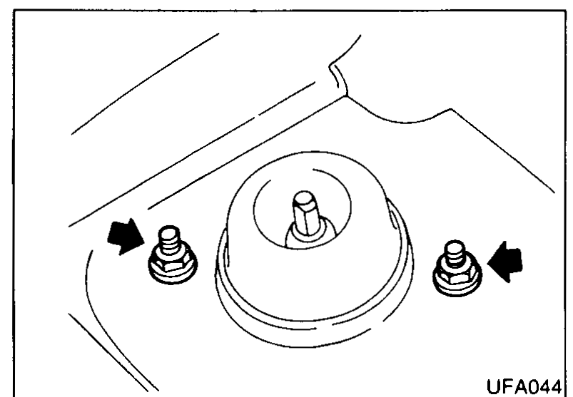 Top view inside the front strut tower with the strut insulator visible and two arrows pointing at the upper strut mounting nuts to be removed.