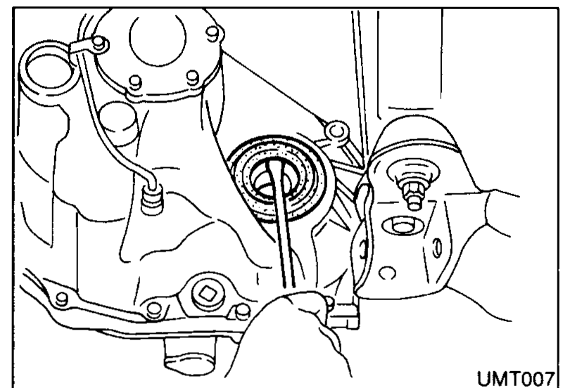 Close-up of the transaxle housing showing a hand using a tool to pry/remove the differential oil seal from its bore. The drain plug area and surrounding casting features are visible.