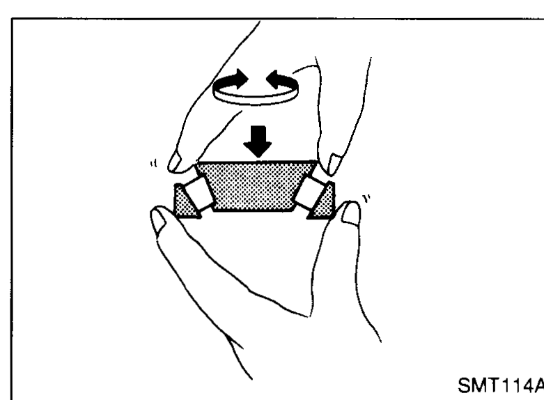Hands holding a tapered roller bearing inner race; arrows highlight a burned-out portion / discoloration to check for.