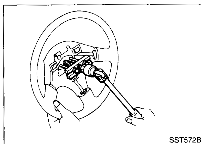 Hands removing the horn pad / horn connections from the steering wheel hub.